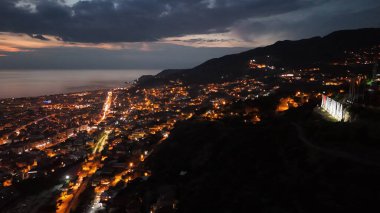Türkiye 'nin Alanya kentinin insansız hava aracı tarafından ele geçirilmiş bir panoraması, aydınlık kenti, yarımadasını ve limanı sakin bir deniz ve alacakaranlık gökyüzüne karşı gösteriyor.