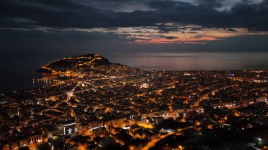 Türkiye 'nin Alanya kentinin insansız hava aracı tarafından ele geçirilmiş bir panoraması, aydınlık kenti, yarımadasını ve limanı sakin bir deniz ve alacakaranlık gökyüzüne karşı gösteriyor.