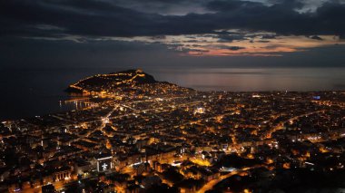 Türkiye 'nin Alanya kentinin insansız hava aracı tarafından ele geçirilmiş bir panoraması, aydınlık kenti, yarımadasını ve limanı sakin bir deniz ve alacakaranlık gökyüzüne karşı gösteriyor.