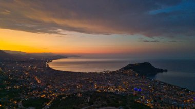 Türkiye 'nin Alanya kentinin hava panoramik manzarası, gün doğumunda hafif aydınlatılmış şehir manzarası, kıvrımlı kıyı şeridi ve sakin Akdeniz koyunu gösteriyor