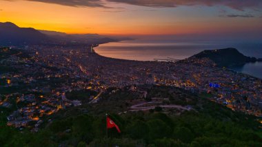 Türkiye 'nin Alanya kentinin hava panoramik manzarası, gün doğumunda hafif aydınlatılmış şehir manzarası, kıvrımlı kıyı şeridi ve sakin Akdeniz koyunu gösteriyor