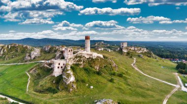 Polonya 'nın Çek Cumhuriyeti yakınlarındaki Olsztyn Kalesi' nin insansız hava aracı görüntüsü sıcak altın saat ışığıyla aydınlatılıyor. Jura Krakowsko-Çekoslovakya manzarasında küçük bir kasabanın üzerinde yükselen ortaçağ kireçtaşı kalesi.
