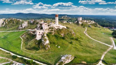 Polonya 'nın Çek Cumhuriyeti yakınlarındaki Olsztyn Kalesi' nin insansız hava aracı görüntüsü sıcak altın saat ışığıyla aydınlatılıyor. Jura Krakowsko-Çekoslovakya manzarasında küçük bir kasabanın üzerinde yükselen ortaçağ kireçtaşı kalesi.