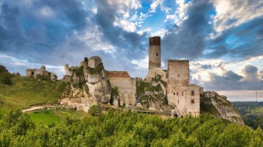 Polonya 'nın Çek Cumhuriyeti yakınlarındaki Olsztyn Kalesi' nin insansız hava aracı görüntüsü sıcak altın saat ışığıyla aydınlatılıyor. Jura Krakowsko-Çekoslovakya manzarasında küçük bir kasabanın üzerinde yükselen ortaçağ kireçtaşı kalesi.