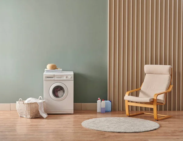 Washing machine in the room, green wall background, laundry interior, detergent and decorative armchair.