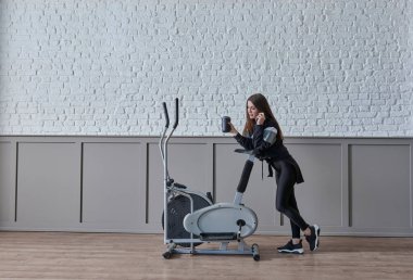 Kadın ev konsepti üzerine spor yapıyor, cep telefonu içme suyu ile konuşuyor, dekoratif arka plan tarzı iç mekan tarzı..