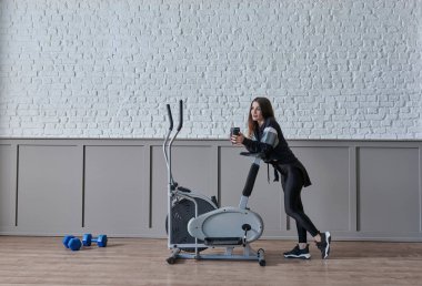 Kadın ev konsepti üzerine spor yapıyor, cep telefonu içme suyu ile konuşuyor, dekoratif arka plan tarzı iç mekan tarzı..