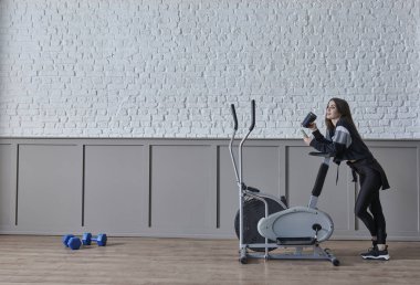 Kadın ev konsepti üzerine spor yapıyor, cep telefonu içme suyu ile konuşuyor, dekoratif arka plan tarzı iç mekan tarzı..