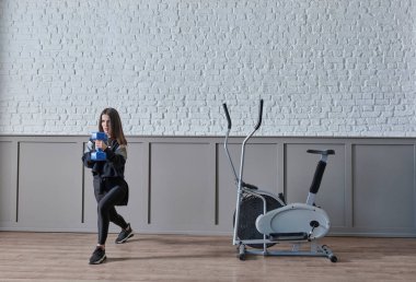 Güzel bir kadın evde dambılla spor yapıyor. Antrenman odası tarzı..