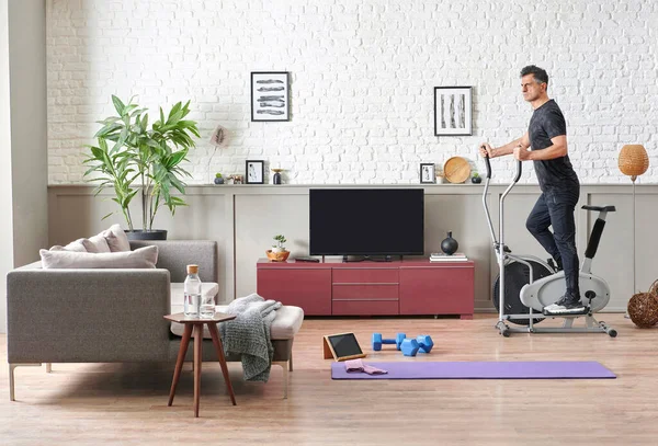 Man is doing sport at home, fit male training style, decorative living room, brick wall sofa and television unit style.