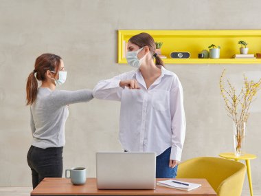 Virüs ve salgın sırasında iş yerinde karşılayan iki kadın meslektaşı. Sosyal uzaklık kavramı.
