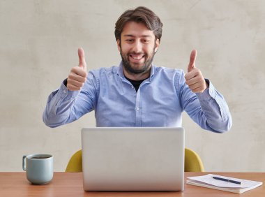 Mavi gömlekli adam dizüstü bilgisayarın, video konuşmasının, gri duvar arkaplanının, sarı kitaplığın, kahve dizüstü bilgisayarının,.