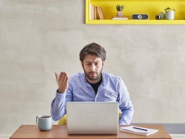 Kızgın adam laptopun önünde video konuşuyor. Gri taş duvar konsepti..