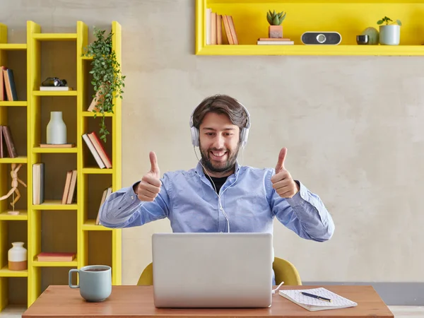 Mavi gömlekli adam dizüstü bilgisayarın, video konuşmasının, gri duvar arkaplanının, sarı kitaplığın, kahve dizüstü bilgisayarının,.