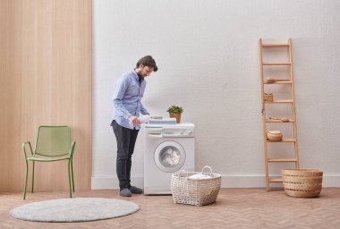 Laundry room washing machine and dirty clothes decorative modern style. Man is filling detergent to the machine.