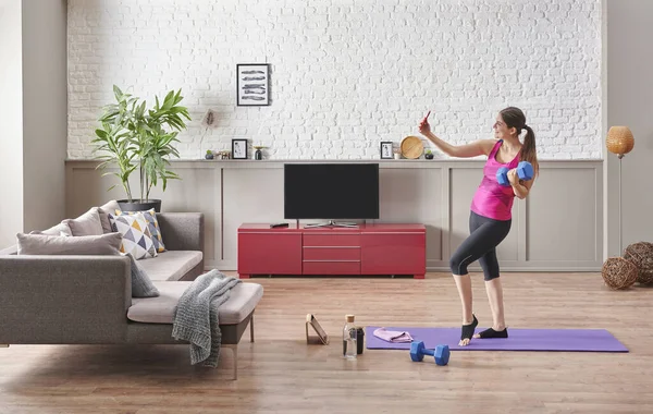 Sportive woman is doing training at home, purple mat, blue dumbbell, decorative living room concept. Healthy lifestyle.