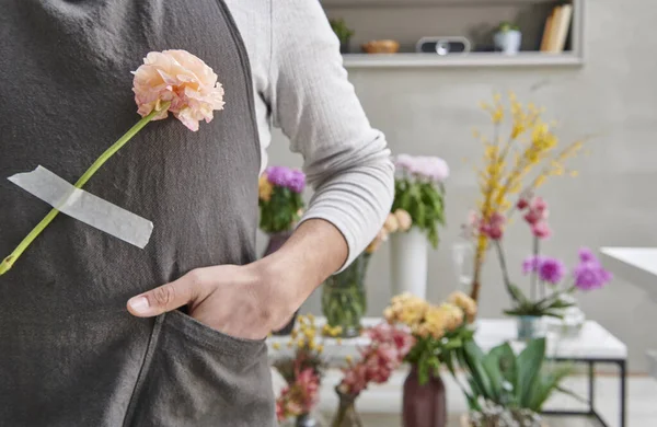 Florist man close up hang flower to the apron, shop background.