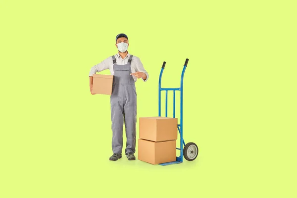 Stock image Delivery and transporter man is holding cardboard box and blue hand truck colorful background.