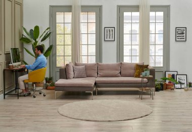 Adam evden, masa bilgisayarından, dekoratif oturma odasından çalışıyor..