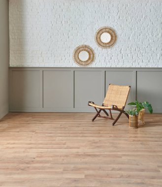 Beyaz tuğla ve kahverengi duvarın önündeki hasır sandalye, ayna ve bitkisel altın vazo.