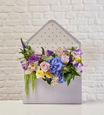 Güzel çiçek aranjmanları: portakal ve beyaz güllerden oluşan bir buket ve beyaz bir duvara karşı dekoratif çizgili bir kutuda pembe bir lale düzeneği..