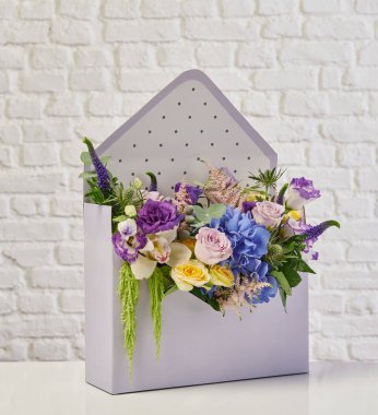 Güzel çiçek aranjmanları: portakal ve beyaz güllerden oluşan bir buket ve beyaz bir duvara karşı dekoratif çizgili bir kutuda pembe bir lale düzeneği..