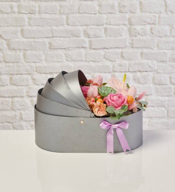 Güzel çiçek aranjmanları: portakal ve beyaz güllerden oluşan bir buket ve beyaz bir duvara karşı dekoratif çizgili bir kutuda pembe bir lale düzeneği..