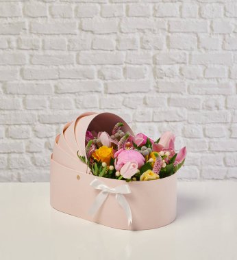 Güzel çiçek aranjmanları: portakal ve beyaz güllerden oluşan bir buket ve beyaz bir duvara karşı dekoratif çizgili bir kutuda pembe bir lale düzeneği..