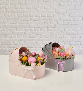 Güzel çiçek aranjmanları: portakal ve beyaz güllerden oluşan bir buket ve beyaz bir duvara karşı dekoratif çizgili bir kutuda pembe bir lale düzeneği..