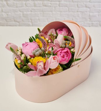 Güzel çiçek aranjmanları: portakal ve beyaz güllerden oluşan bir buket ve beyaz bir duvara karşı dekoratif çizgili bir kutuda pembe bir lale düzeneği..