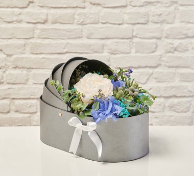 Güzel çiçek aranjmanları: portakal ve beyaz güllerden oluşan bir buket ve beyaz bir duvara karşı dekoratif çizgili bir kutuda pembe bir lale düzeneği..