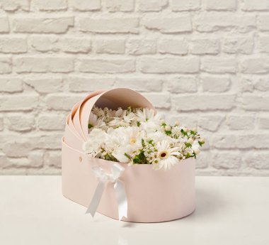 Güzel çiçek aranjmanları: portakal ve beyaz güllerden oluşan bir buket ve beyaz bir duvara karşı dekoratif çizgili bir kutuda pembe bir lale düzeneği..