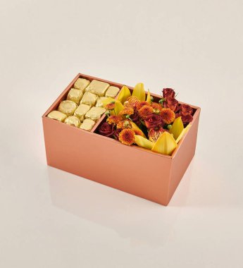 Güzel çiçek aranjmanları: portakal ve beyaz güllerden oluşan bir buket ve beyaz bir duvara karşı dekoratif çizgili bir kutuda pembe bir lale düzeneği..