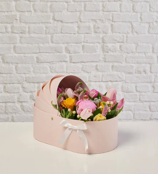 Güzel çiçek aranjmanları: portakal ve beyaz güllerden oluşan bir buket ve beyaz bir duvara karşı dekoratif çizgili bir kutuda pembe bir lale düzeneği..