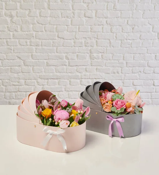 Güzel çiçek aranjmanları: portakal ve beyaz güllerden oluşan bir buket ve beyaz bir duvara karşı dekoratif çizgili bir kutuda pembe bir lale düzeneği..