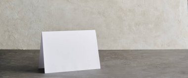 Tarafsız bir zemin üzerinde duran boş katlanmış bir kartın olduğu minimalist modelleme sahnesi, davetiyeleri göstermek için ideal, tebrik kartı tasarımları, markalaşma veya promosyon şablonları.