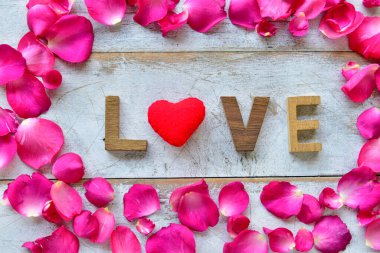 Çiçek kompozisyonu. Aşk sözcüğü ahşap kalpten ve tahta arka planda gül yapraklarından oluşur. Sevgililer Günü konsepti.