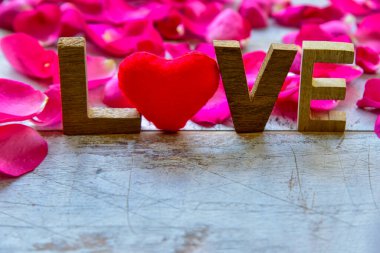 Çiçek kompozisyonu. Aşk sözcüğü ahşap kalpten ve tahta arka planda gül yapraklarından oluşur. Sevgililer Günü konsepti.