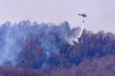 Helikopter engebeli bir arazide orman yangınına su bırakıyor.