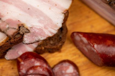 Tütsülenmiş göğüs eti, tahıllı ekmek ve ahşap kesim tahtasındaki ev yapımı sosis. Yakın çekim, seçici odaklanma.