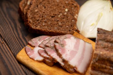 Tütsülenmiş göğüs eti ve ahşap kesim tahtasının üzerinde tahıllı ekmek. Yakın çekim, seçici odaklanma.