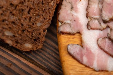 Tütsülenmiş göğüs eti ve ahşap kesim tahtasının üzerinde tahıllı ekmek. Yakın çekim, seçici odaklanma.