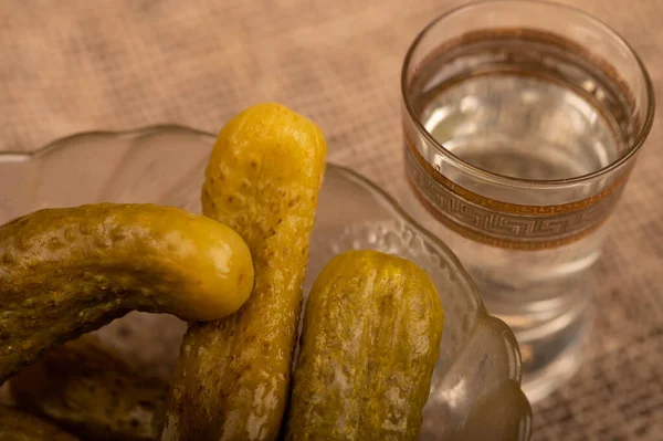 一杯伏特加酒和腌制黄瓜 放在玻璃器皿里 背景是粗糙质感的自制织物 特选重点 — 图库照片
