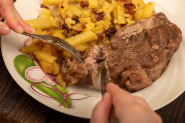 Birisi çatal ve bıçakla bir tabak kızarmış patatesle sulu bir parça et kesiyor. Seçici Odaklamayı Kapat