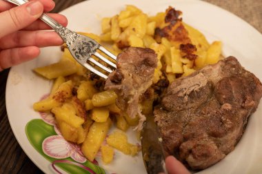 Birisi çatal ve bıçakla bir tabak kızarmış patatesle sulu bir parça et kesiyor. Seçici Odaklamayı Kapat