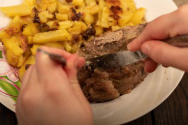 Birisi çatal ve bıçakla bir tabak kızarmış patatesle sulu bir parça et kesiyor. Seçici Odaklamayı Kapat