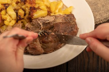 Birisi çatal ve bıçakla bir tabak kızarmış patatesle sulu bir parça et kesiyor. Seçici Odaklamayı Kapat