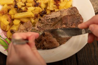 Birisi çatal ve bıçakla bir tabak kızarmış patatesle sulu bir parça et kesiyor. Seçici Odaklamayı Kapat