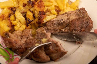 Birisi çatal ve bıçakla bir tabak kızarmış patatesle sulu bir parça et kesiyor. Seçici Odaklamayı Kapat