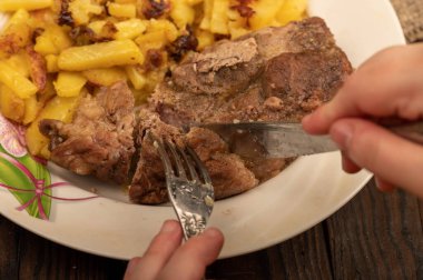 Birisi çatal ve bıçakla bir tabak kızarmış patatesle sulu bir parça et kesiyor. Seçici Odaklamayı Kapat